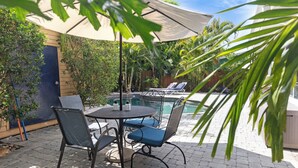 Un espace extérieur aménagé avec une piscine, une table entourée de chaises et un coin salon abrité.