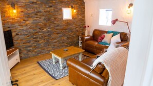 Een gezellige woonkamer met een stenen muur, houten vloeren, een bruine leren bank, een houten salontafel en een tv-meubel.