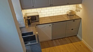 Una cucina compatta con mobili bianchi, un forno a microonde, un tostapane e una lavastoviglie.