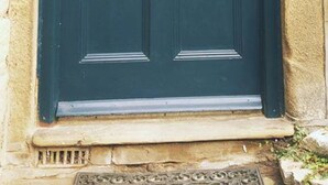 Una porta blu scuro con una basetta di ottone e una fessura per la posta, incastonata in un muro di pietra.