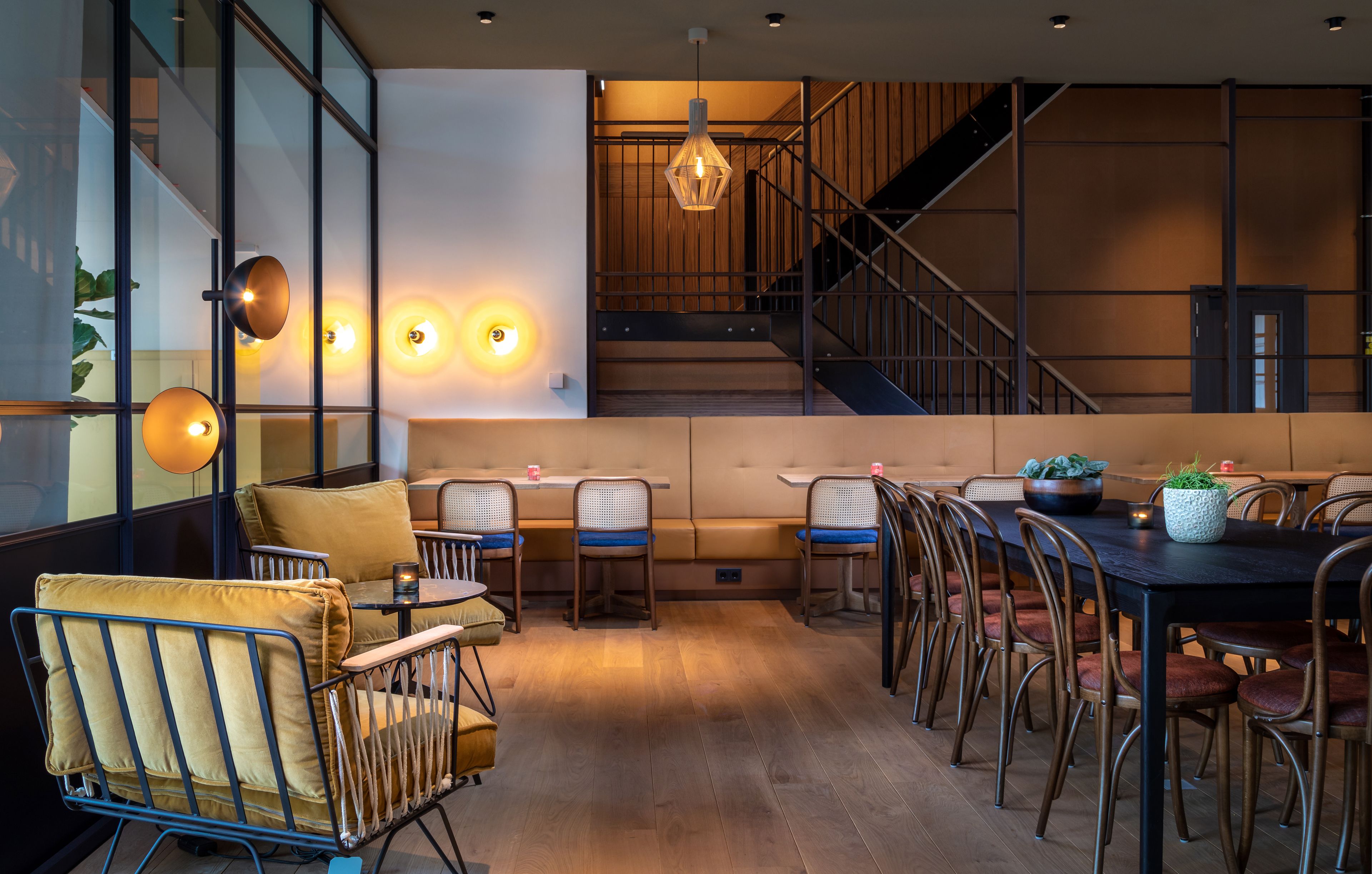 A modern dining area with a long table, multiple chairs, and a staircase in the background.