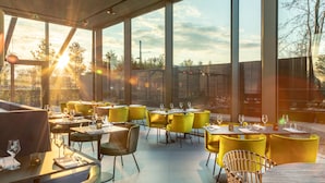 A restaurant with large windows, yellow chairs, and tables set for dining.