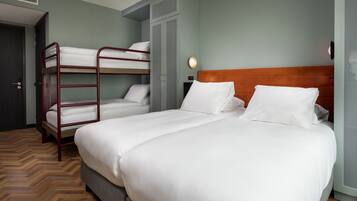 A hotel room with a bunk bed, a single bed, a wooden headboard, a wall-mounted light, and a door.