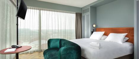 Quarto de hotel com uma cama, escrivaninha, cadeira e televisão.