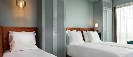 A hotel room with two beds, a wardrobe, and a bedside table with a lamp.