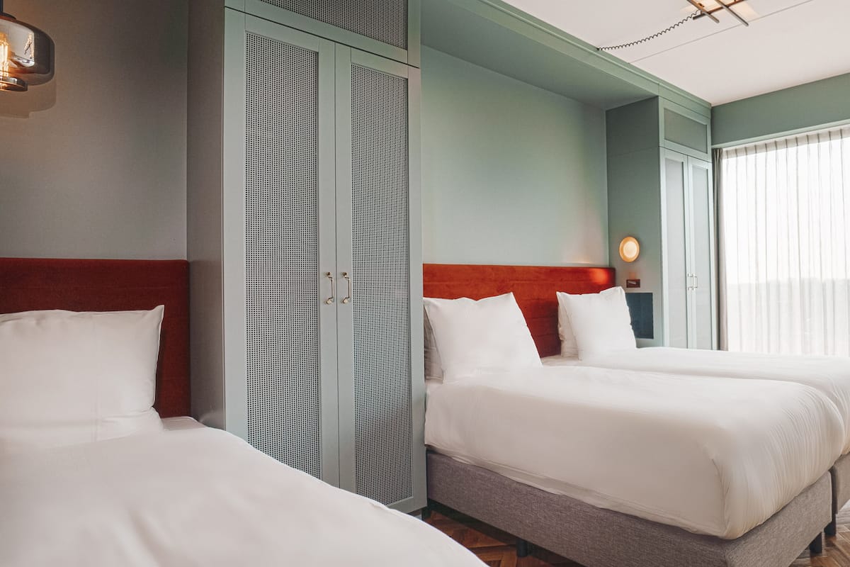 A hotel room with two beds, a wardrobe, and a ceiling fan.