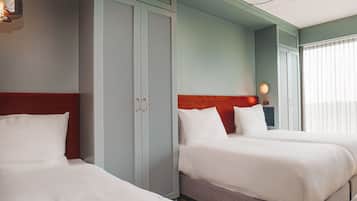 A hotel room with two beds, a wardrobe, and a ceiling fan.