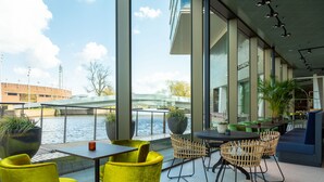 A modern outdoor seating area with yellow chairs and tables, overlooking a river with a bridge in the background.