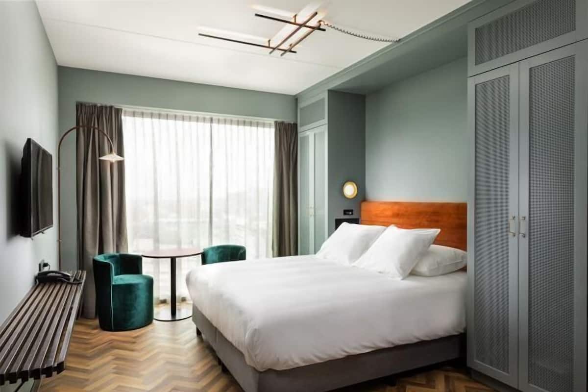 A hotel room with a bed, a desk, a chair, a TV, and a wardrobe.