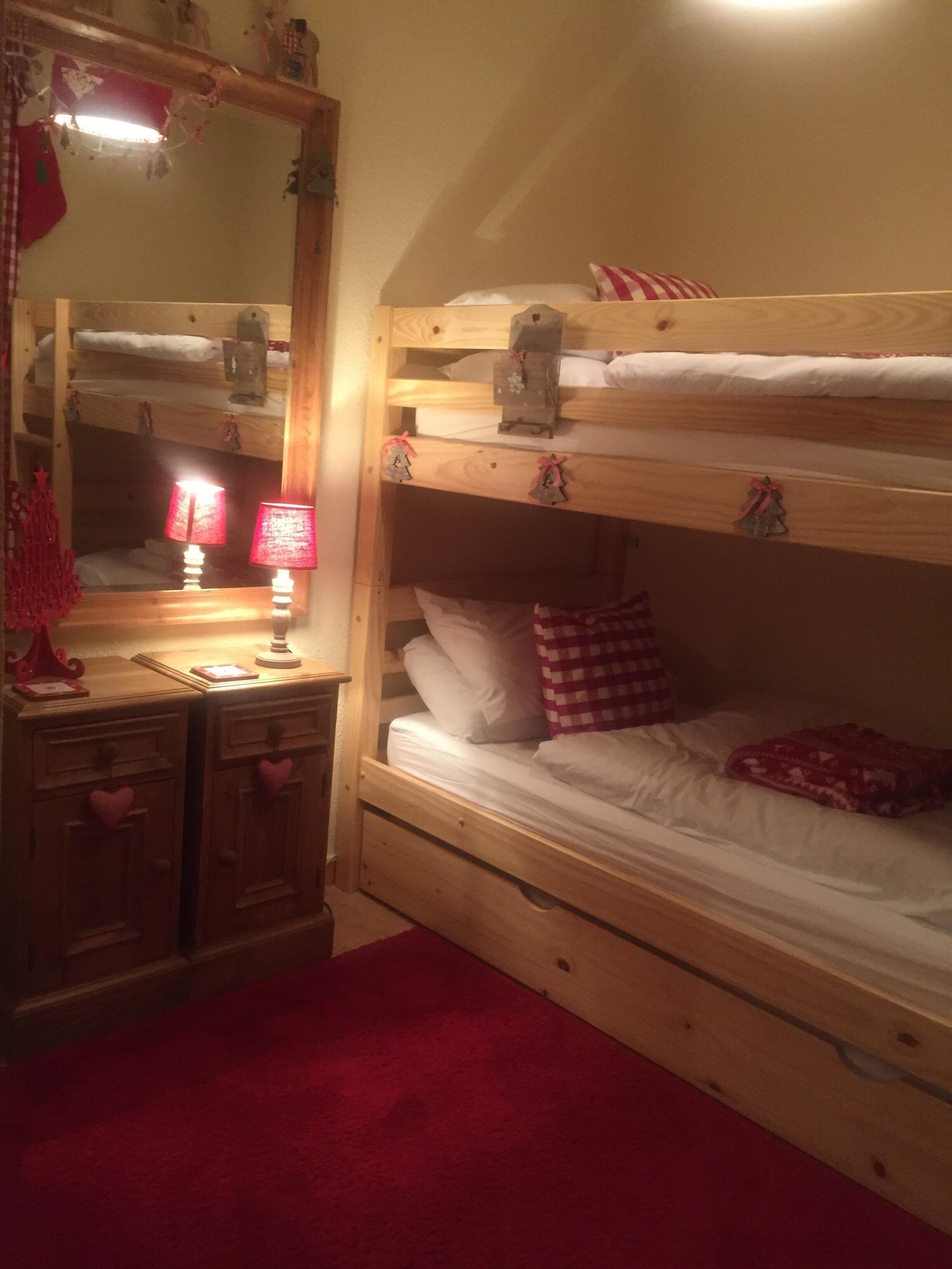 Une chambre avec un lit superposé, une commode en bois, un miroir et une moquette rouge.