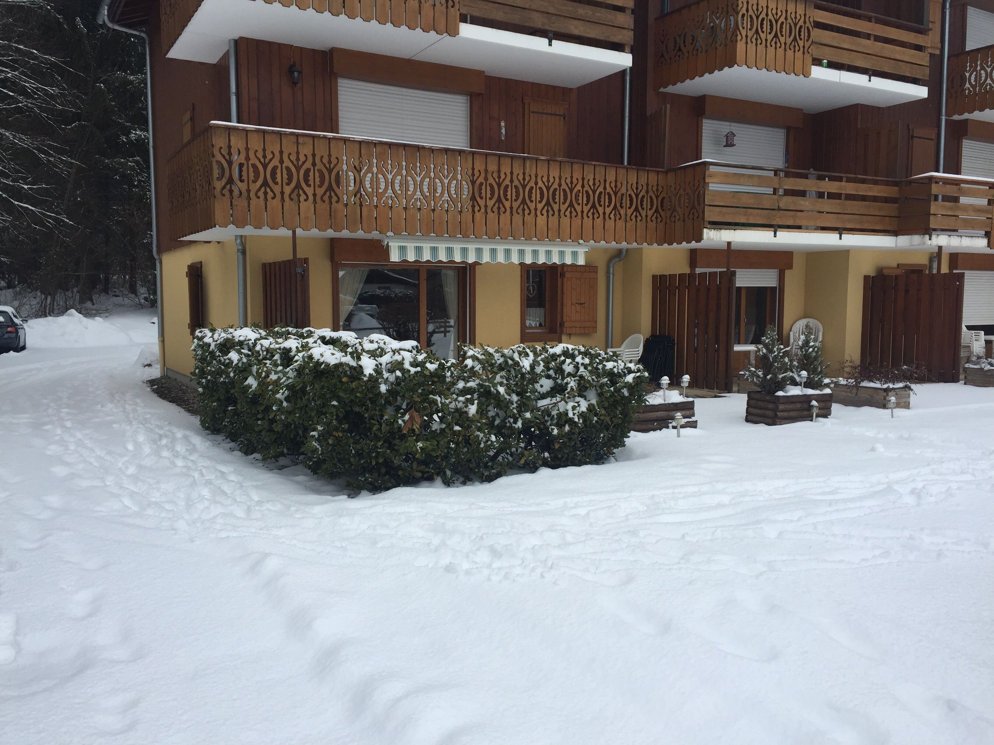 Un bâtiment à deux étages doté d’un balcon, d’un jardin recouvert de neige et d’une voiture garée.