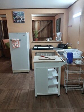 A compact kitchen with a refrigerator, a small countertop, and a metal rack with dishes. - Raindrops Apartments (Monteverde)