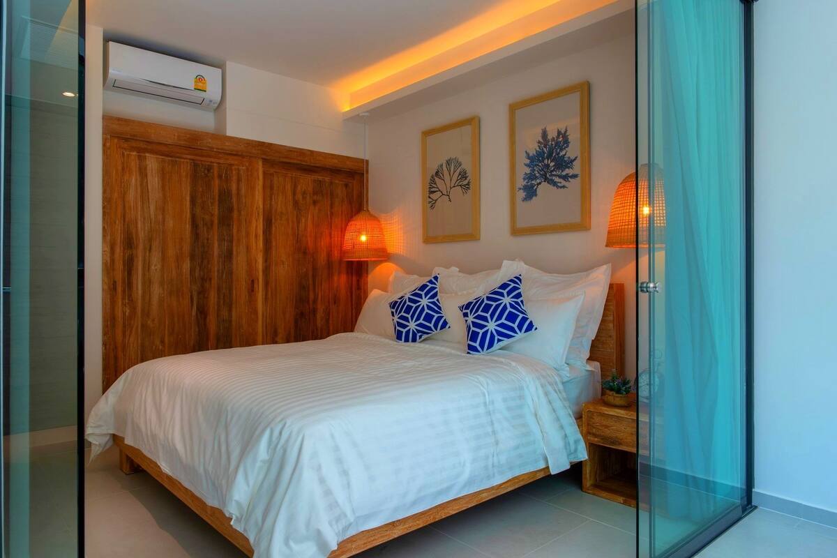 Een slaapkamer met een houten bedframe, witte beddengoed en twee blauw gestreepte kussens.