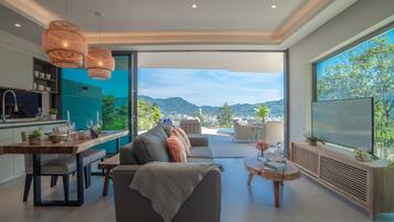 Una sala de estar moderna con un sofá, una mesa de comedor y vistas a un paisaje urbano a través de amplios ventanales.