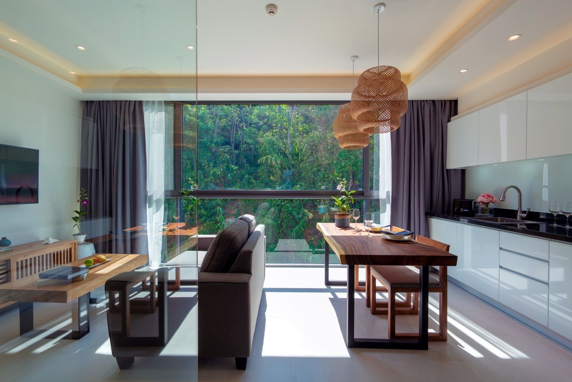 A modern kitchen with a dining area, large windows, and a view of greenery.