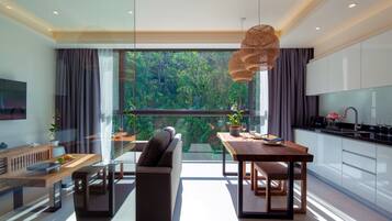 A modern kitchen with a dining area, large windows, and a view of greenery.