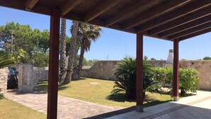 Un patio cubierto con suelo de piedra, palmeras y un muro de piedra al fondo.