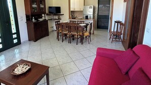Una sala de estar con un sofá rojo, una mesa de centro de madera y un comedor con sillas de madera, con una cocina al fondo.