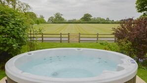A hot tub in a garden with a view of a field and a wooden fence. - The Cotswold Manor Lodge, Exclusive Hot Tub, Games Barn, 70 acres of Parkland (Bampton)