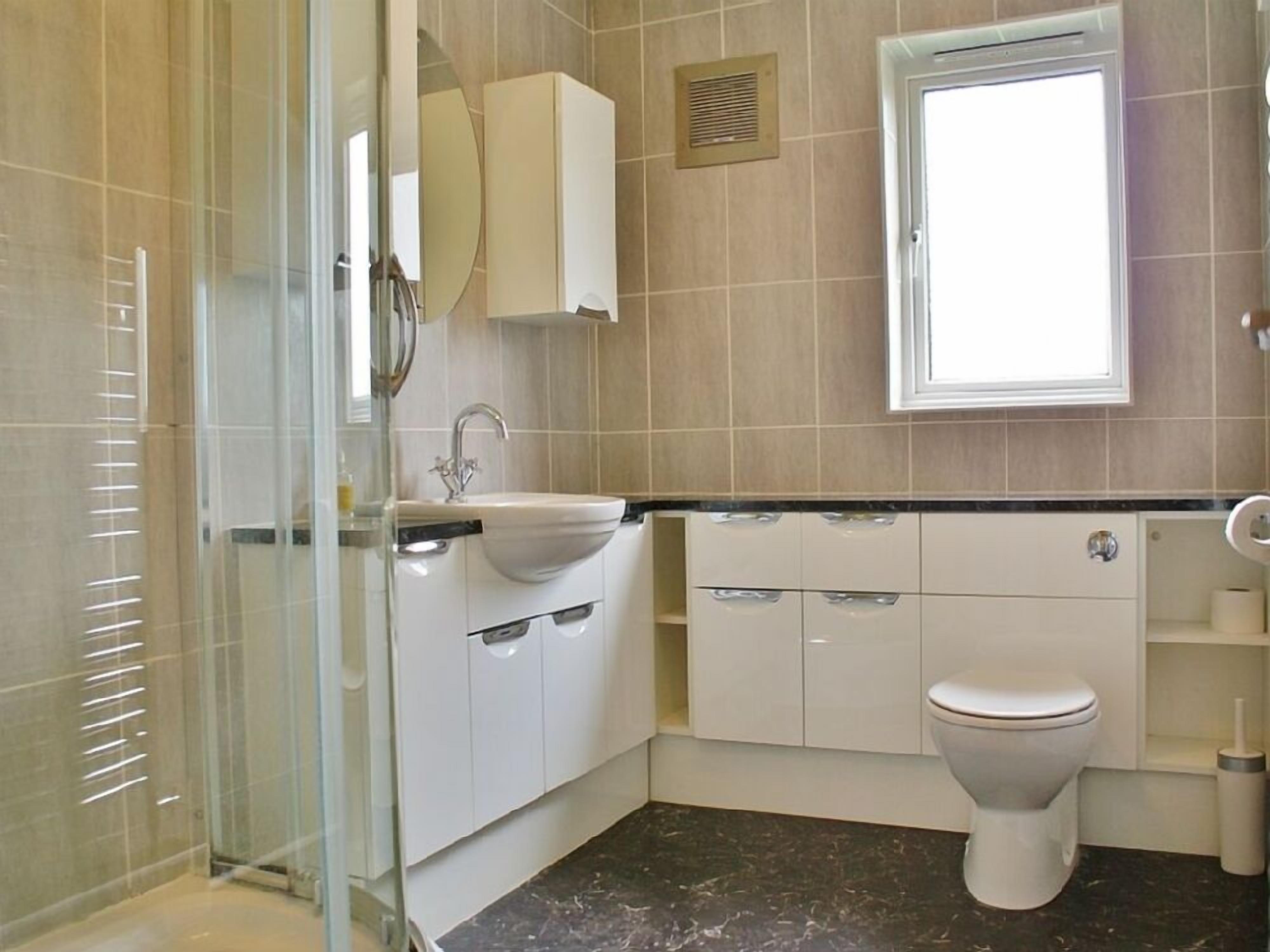 A modern bathroom with a glass shower enclosure, a sink with a faucet, a toilet, and a window providing natural light.