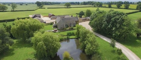 A rural estate with a pond, a pathway, and a large house surrounded by fields and trees.