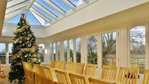 A spacious room with a large Christmas tree, wooden chairs, and a high ceiling with skylights. - The Cotswold Manor Lodge, Exclusive Hot Tub, Games Barn, 70 acres of Parkland (Bampton)