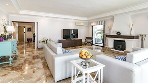 Ein geräumiges Wohnzimmer mit einer großen Couch, einem Fernseher, einem Kamin und einem Couchtisch mit Obst.
