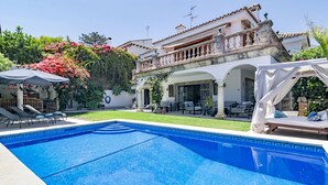 Ein Schwimmbecken mit Liegestühlen und Sonnenschirmen, eine überdachte Terrasse und ein großes Haus mit Balkon.