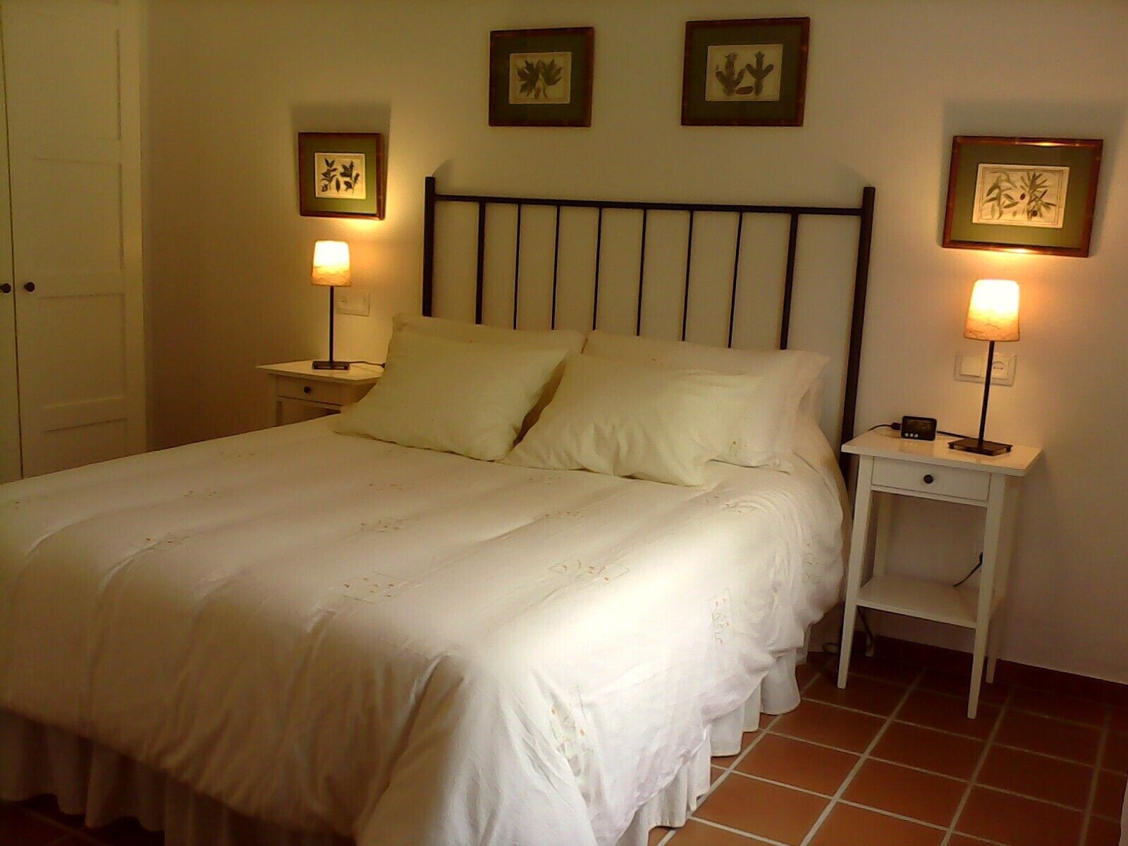 A neatly made bed with white linens, two bedside tables with lamps, and framed artwork on the walls.