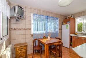 Une cuisine avec un mur recouvert de carreaux, une table en bois avec des chaises, un réfrigérateur et une fenêtre avec un rideau.