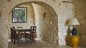 A stone-walled room with a table and chairs, a window with a view of trees, and a lamp on the floor. - Idyllic olive mill with heated pool, in an olive grove, close to sea and Ostuni (Ostuni)