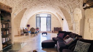 A spacious room with a high arched ceiling, a large window, a sofa, a coffee table, and a bookshelf. - Idyllic olive mill with heated pool, in an olive grove, close to sea and Ostuni (Ostuni)