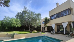 Ein modernes, zweistöckiges Haus mit Pool, Sitzgelegenheiten im Freien und einem gepflegten Garten.