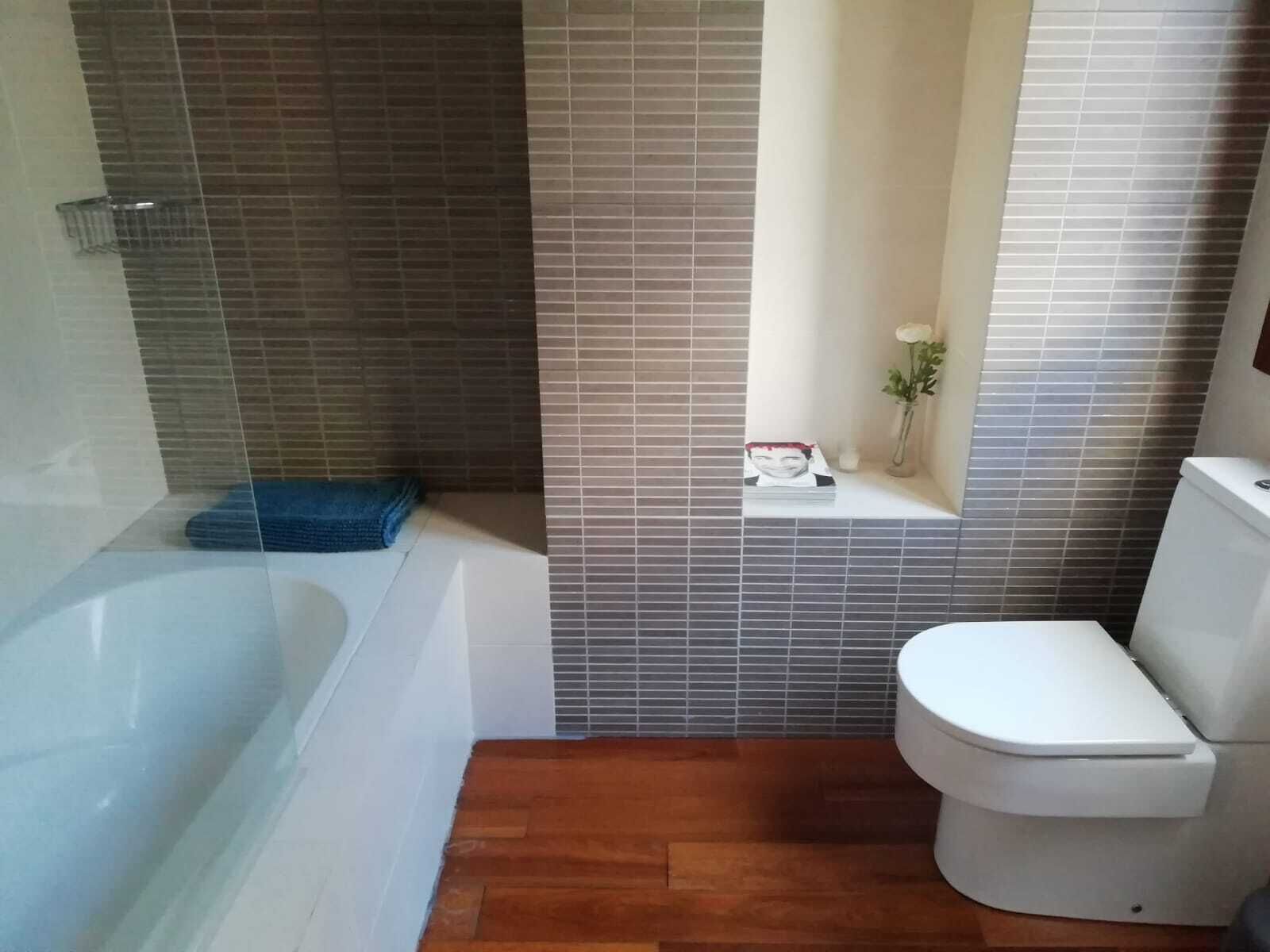 Een badkamer met een bad, toilet en een klein plankje met een vaas en een boek.