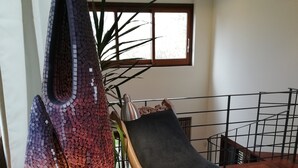 Ein modernes Wohnzimmer mit großem Fenster, einem Hängekorbsessel, einer dekorativen Vase und einem Tablett mit Kerzen.