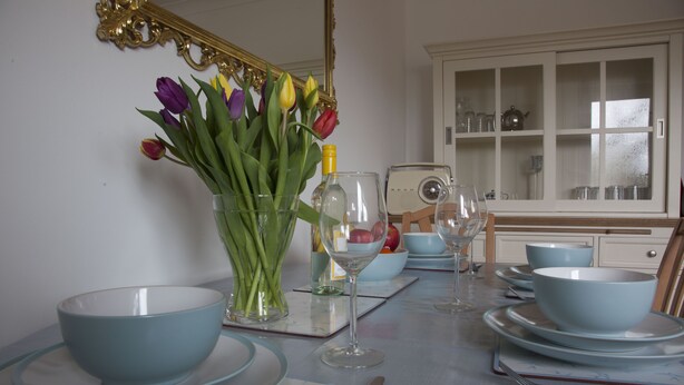 Uma mesa de jantar posta com tigelas, pratos e talheres azuis, um vaso com flores e um rádio.