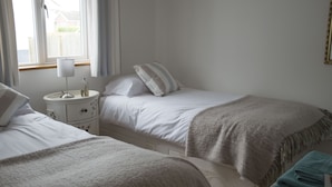 Quarto com duas camas, mesa de cabeceira com abajur, janela com cortinas e vista para o exterior.