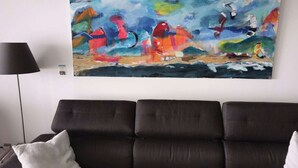 Ett vardagsrum med en mörkbrun soffa, en svart golvlampa och en färgstark, abstrakt tavla på väggen.