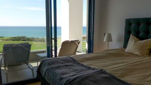 Ett sovrum med en stor säng, utsikt över havet och en balkong med en stol.