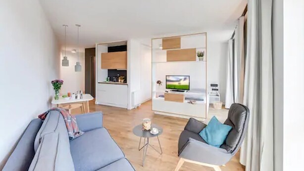 Una sala de estar moderna con un sofá, una butaca, una mesita y una zona de televisión con un televisor de pantalla plana y una planta.