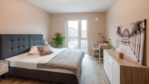 Un dormitorio con cama, mesita de noche, escritorio, silla y un ventanal grande.