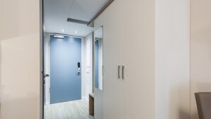 Un pasillo con una puerta azul, paredes blancas y un espejo a la derecha.