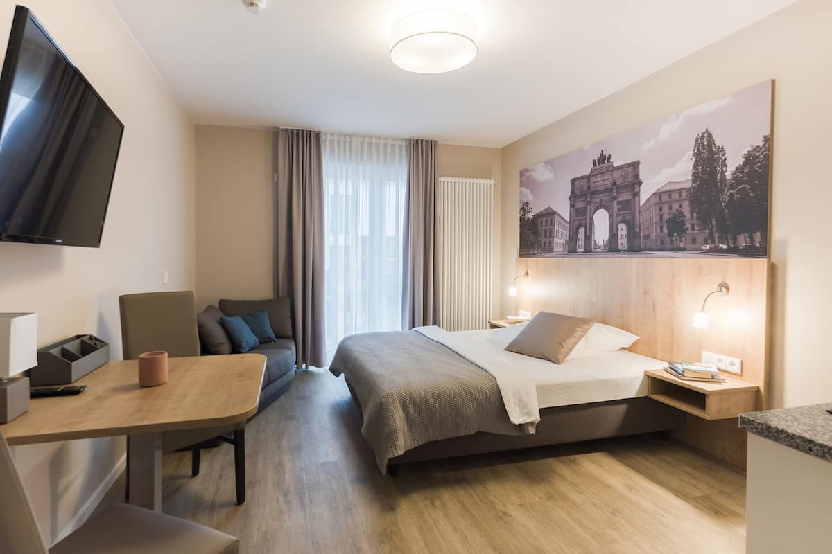 A hotel room with a bed, a desk, a TV, and a painting of a cityscape.