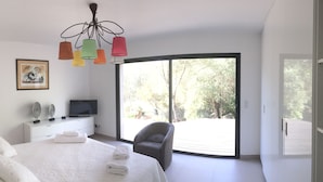 Une chambre à coucher comprenant un lit, une table de chevet, une télévision et une grande fenêtre donnant sur la forêt.