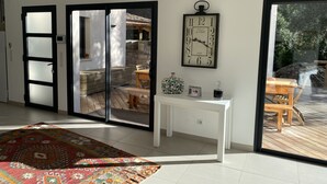 Un intérieur moderne avec une porte-fenêtre coulissante donnant sur un patio, une console blanche et une horloge décorative.