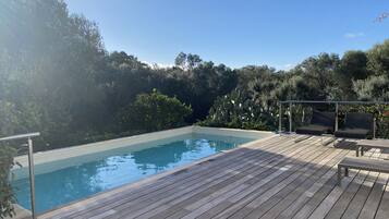 Une terrasse en bois avec une piscine, entourée d’une végétation luxuriante et d’arbres.