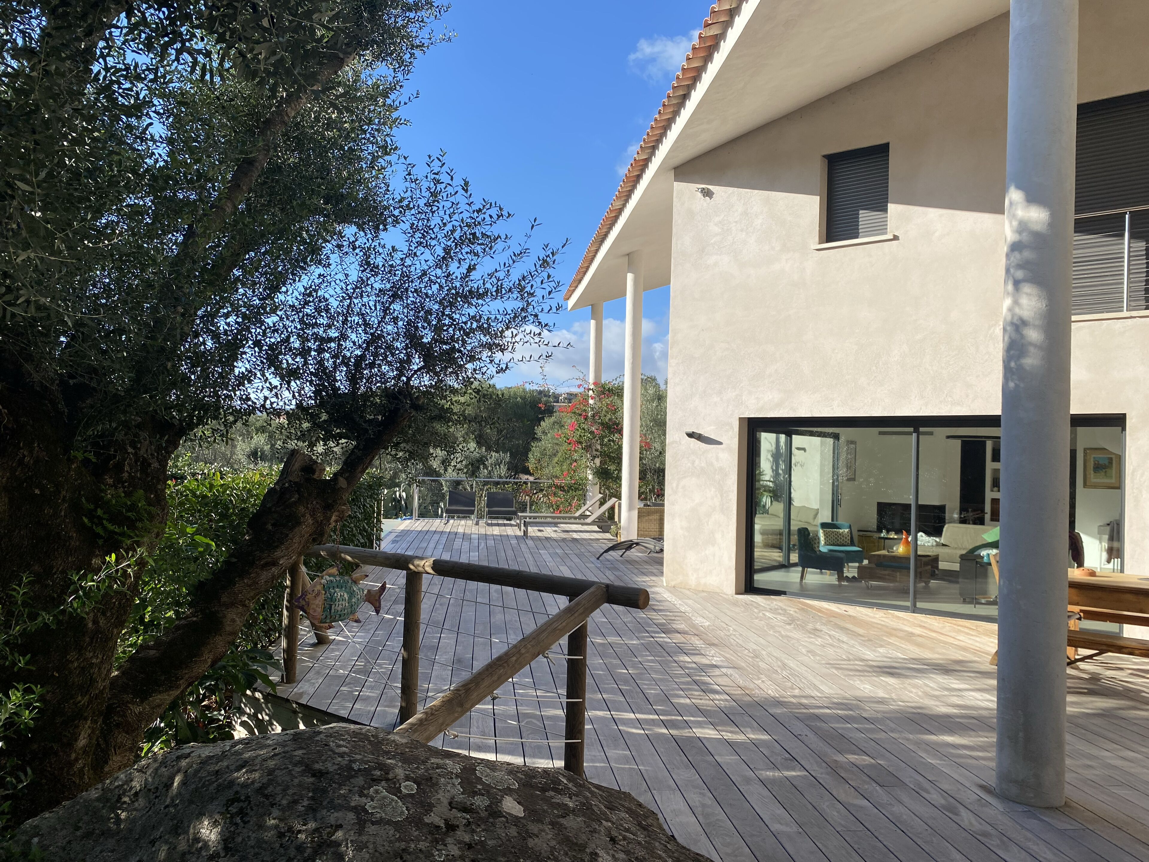 Une maison moderne dotée d’une terrasse en bois, de grandes fenêtres et offrant une vue sur le paysage environnant.
