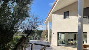 Une maison moderne dotée d’une terrasse en bois, de grandes fenêtres et offrant une vue sur le paysage environnant.