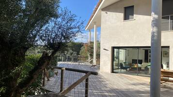 Une maison moderne dotée d’une terrasse en bois, de grandes fenêtres et offrant une vue sur le paysage environnant.