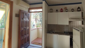 Una cocina compacta con armarios blancos, piso de baldosas y un ventanal pequeño.